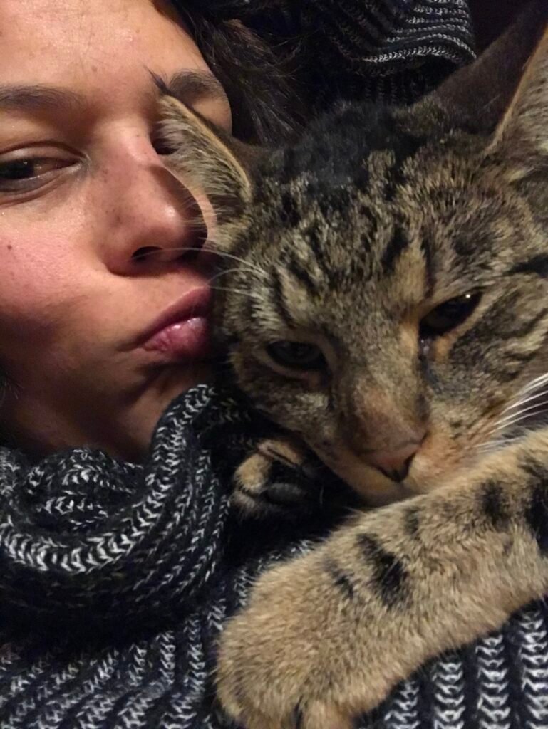 close shot of a woman in grey woolly sweater and a moggy tabby cat snuggling